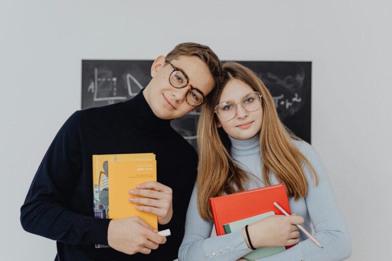 Two students holding books against a blackboard, smiling for the camera, embodying a learning environment.